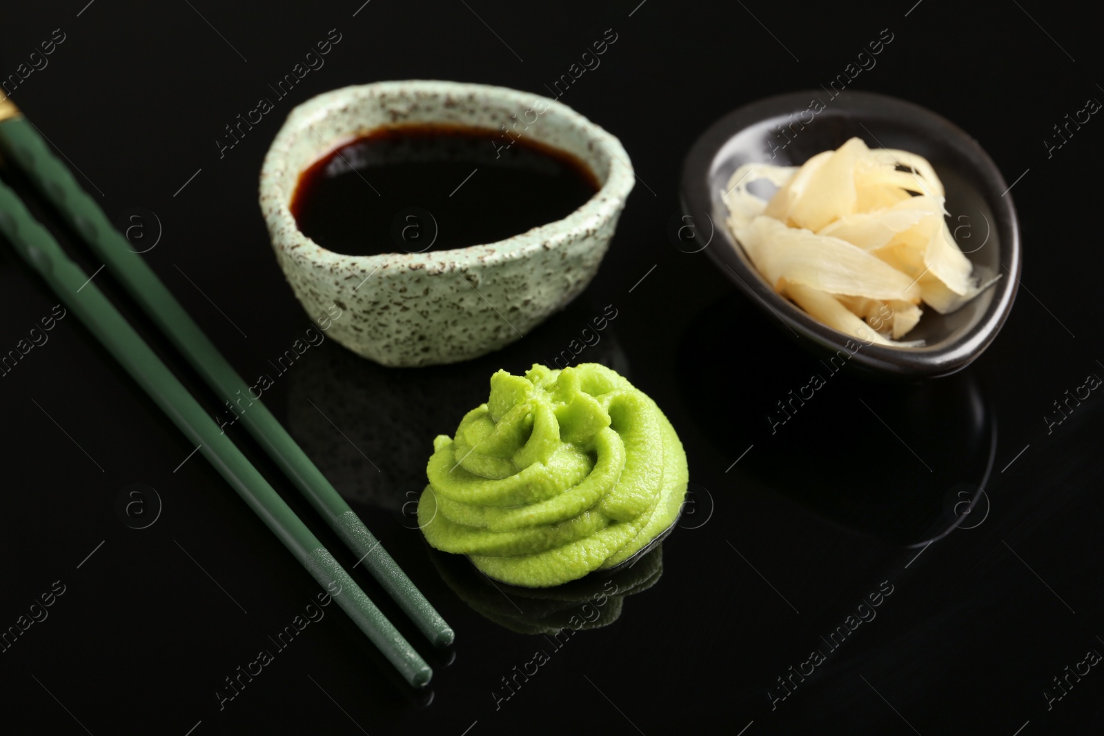 Photo of Hot wasabi paste, soy sauce, ginger and chopsticks on black mirror surface, closeup