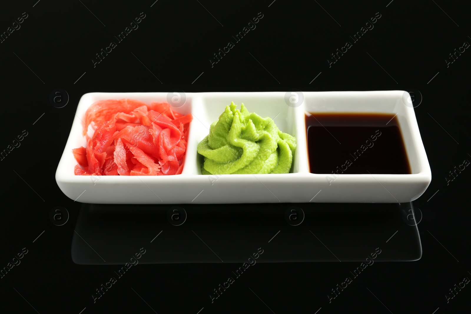 Photo of Hot wasabi paste, soy sauce and ginger on black mirror surface, closeup