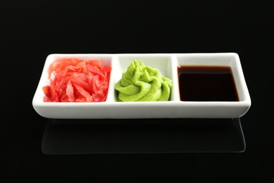 Photo of Hot wasabi paste, soy sauce and ginger on black mirror surface, closeup