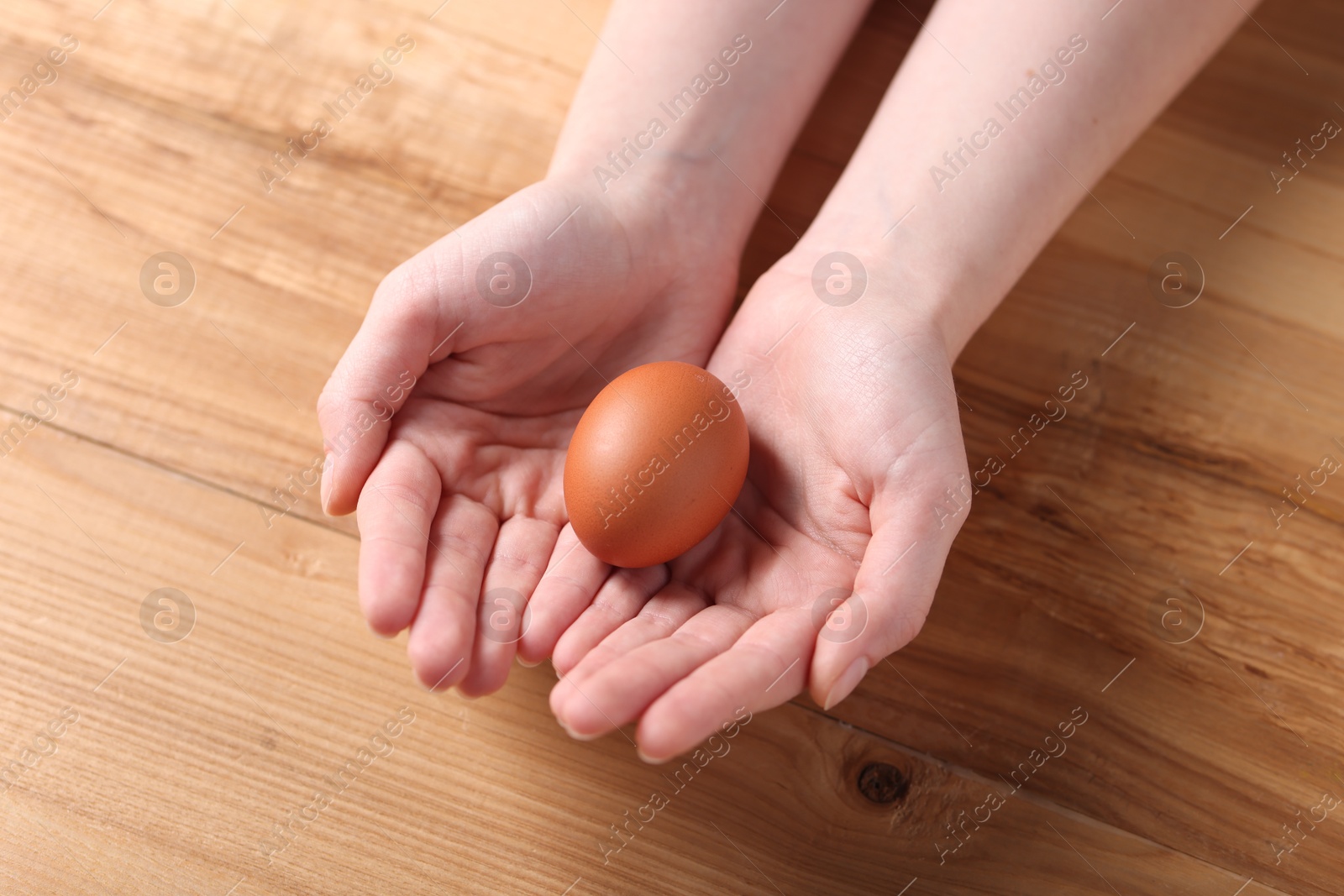 Photo of Woman with raw egg at wooden table, closeup