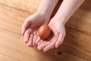 Photo of Woman with raw egg at wooden table, closeup