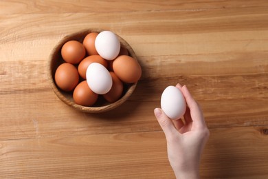 Photo of Woman with raw eggs at wooden table, top view