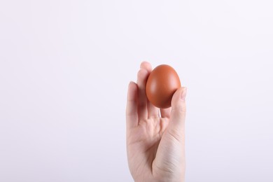 Photo of Woman holding raw egg on light background, closeup. Space for text