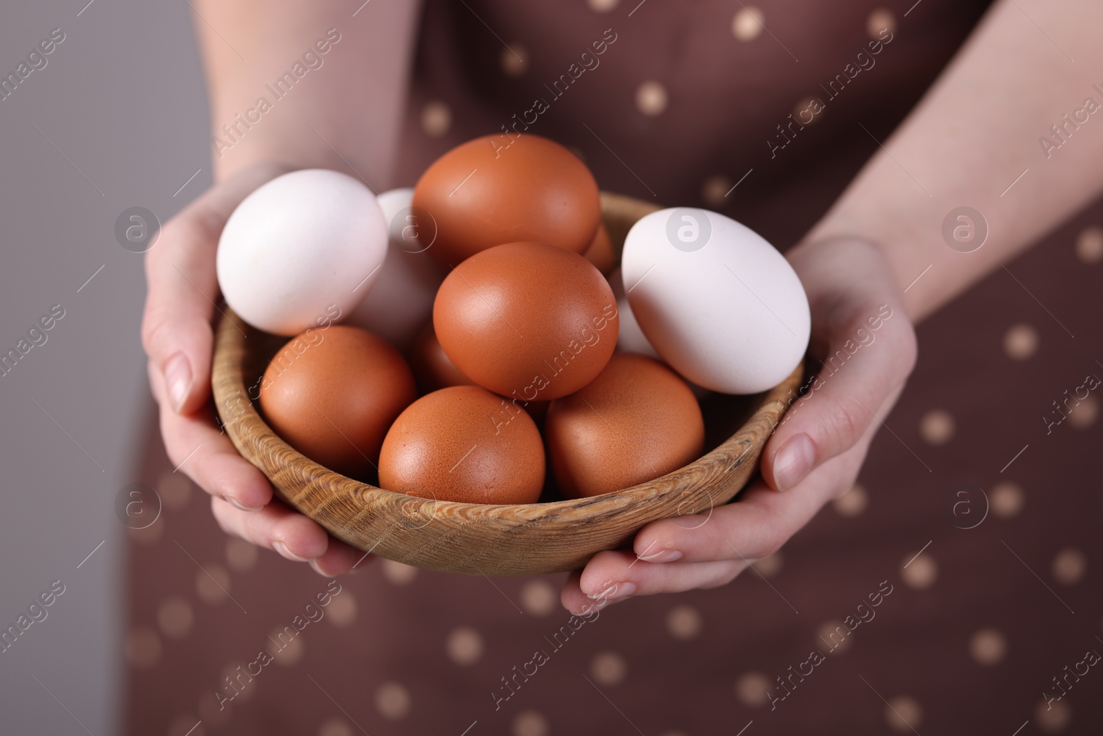 Photo of Woman with bowl of raw eggs on grey background, closeup