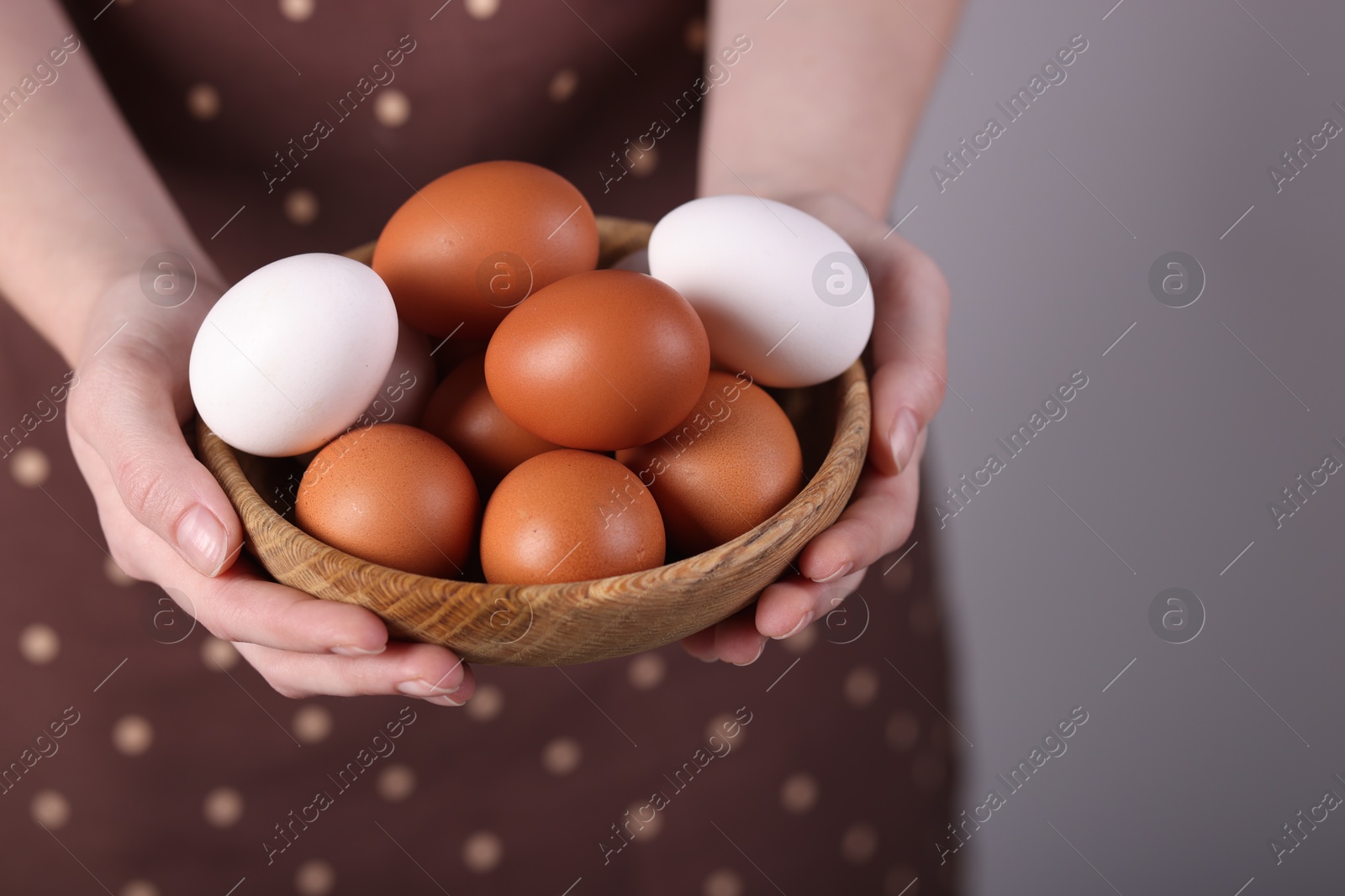 Photo of Woman with bowl of raw eggs on grey background, closeup