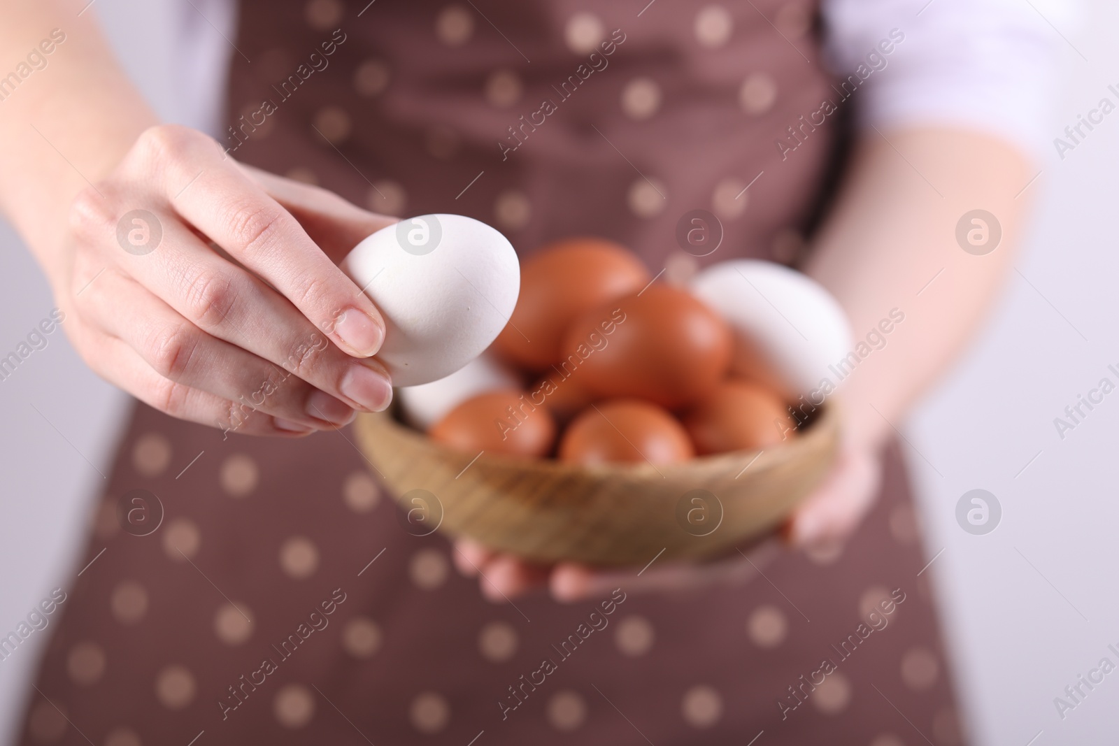 Photo of Woman with bowl of raw eggs on light background, closeup