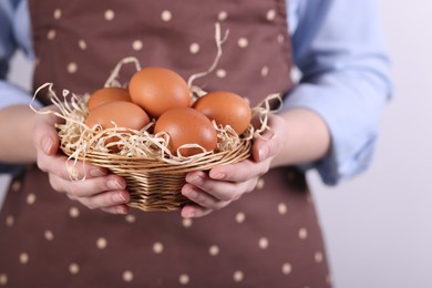 Photo of Woman with basket of raw eggs on light background, closeup