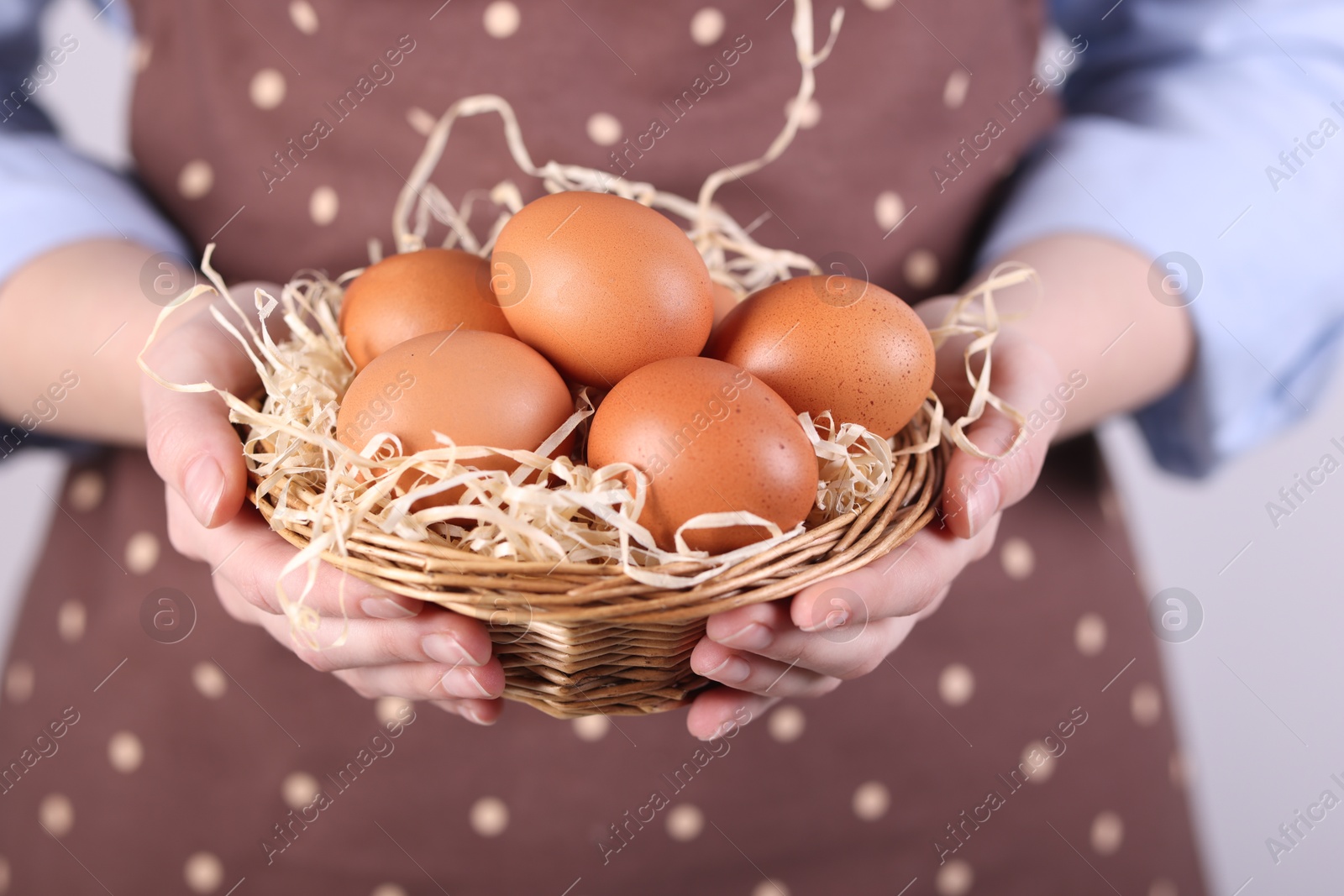 Photo of Woman with basket of raw eggs on light background, closeup