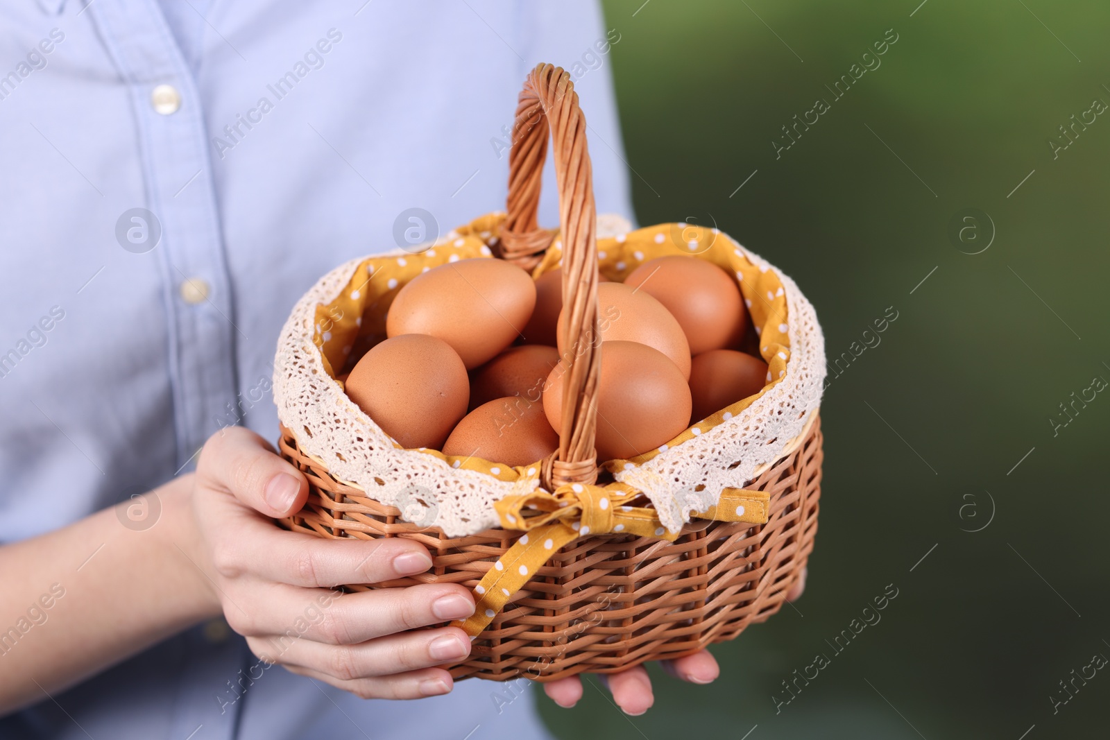 Photo of Woman with basket of raw eggs on blurred background, closeup