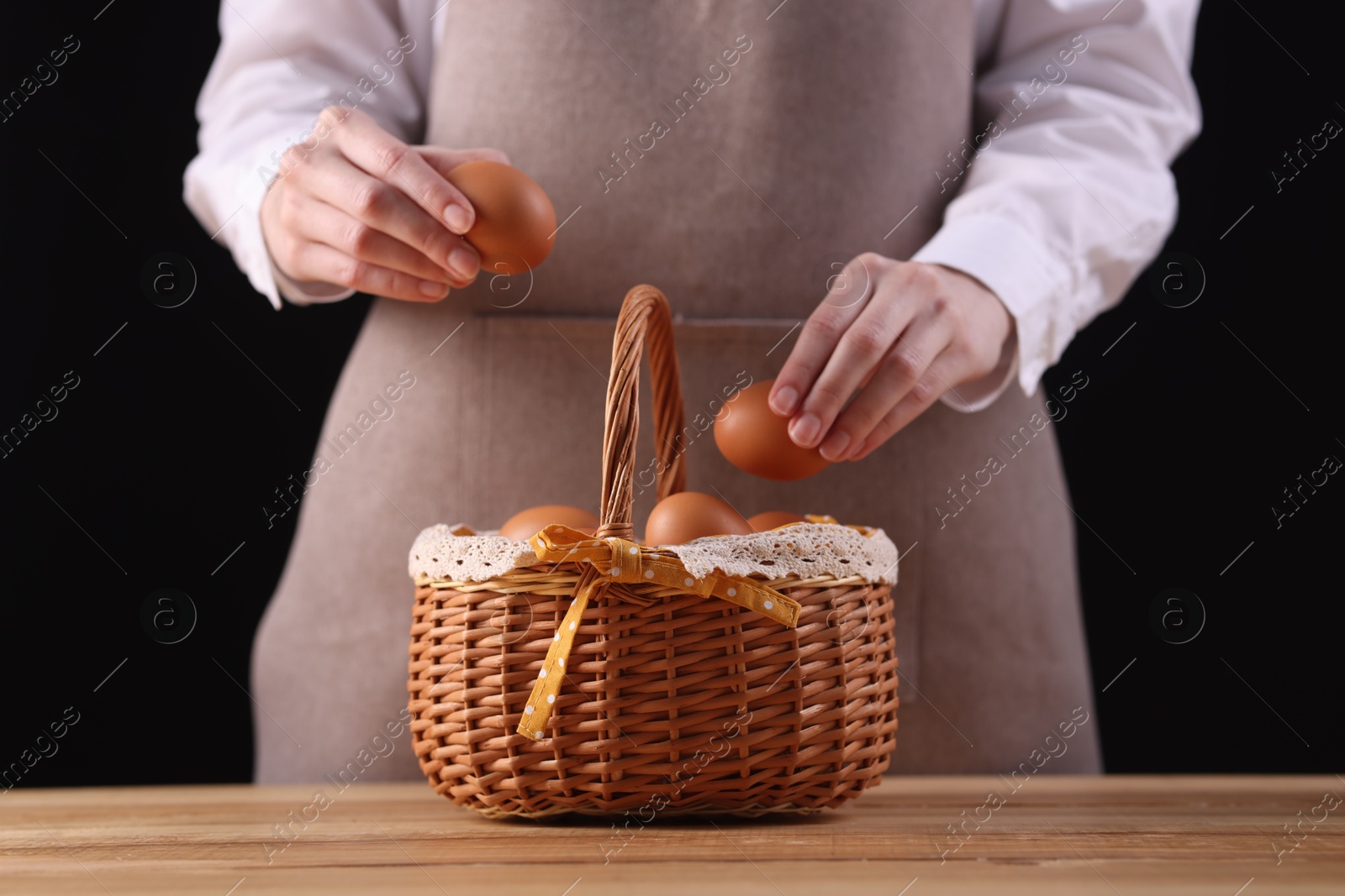 Photo of Woman with basket of raw eggs at wooden table, closeup