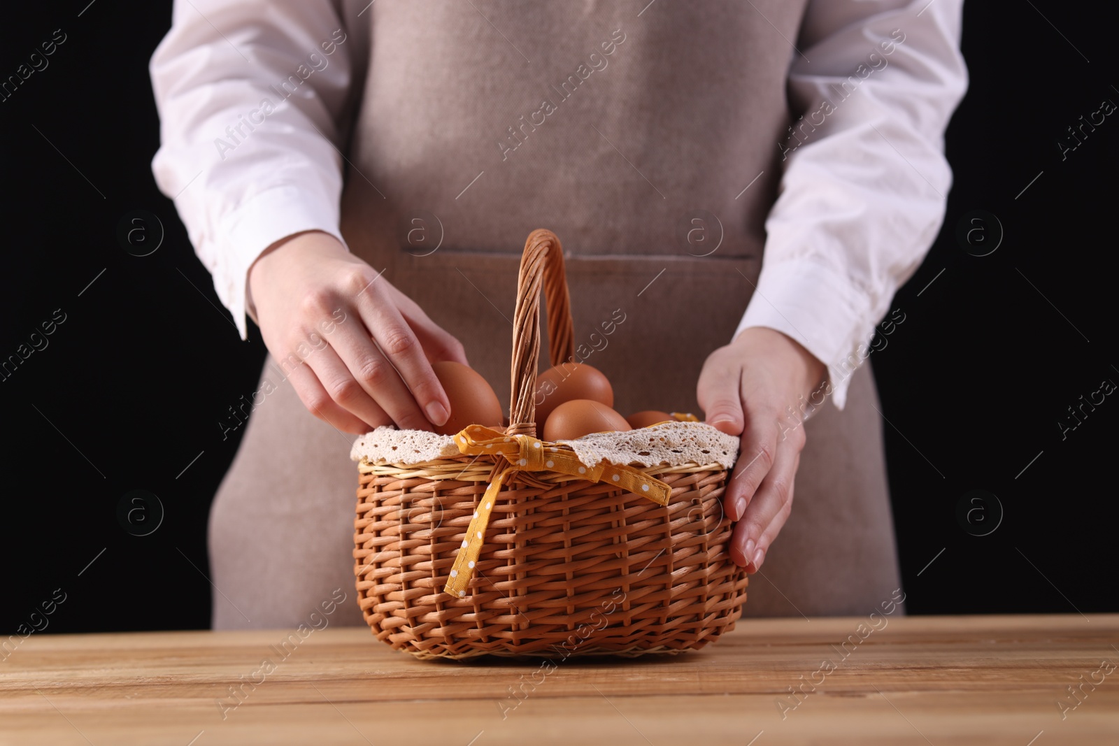 Photo of Woman with basket of raw eggs at wooden table, closeup