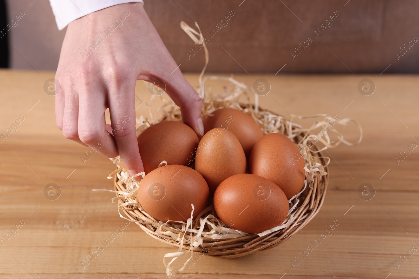 Photo of Woman with basket of raw eggs at wooden table, closeup