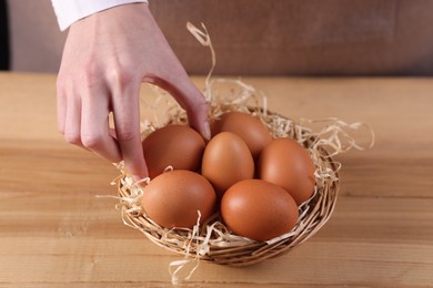 Photo of Woman with basket of raw eggs at wooden table, closeup