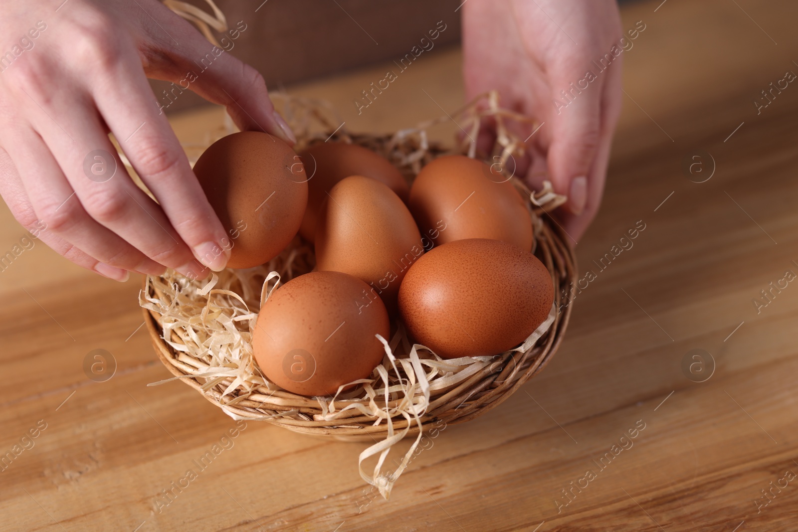 Photo of Woman with basket of raw eggs at wooden table, closeup