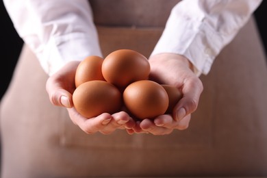 Photo of Woman with raw eggs on dark background, closeup