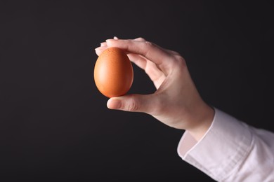 Photo of Woman holding raw egg on black background, closeup