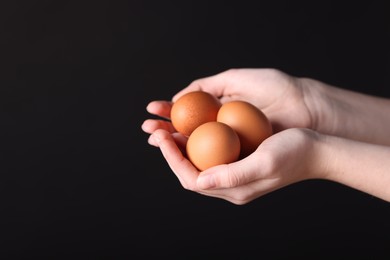 Photo of Woman with raw eggs on black background, closeup. Space for text