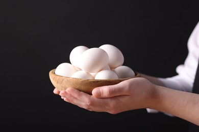 Photo of Woman with bowl of raw eggs on black background, closeup