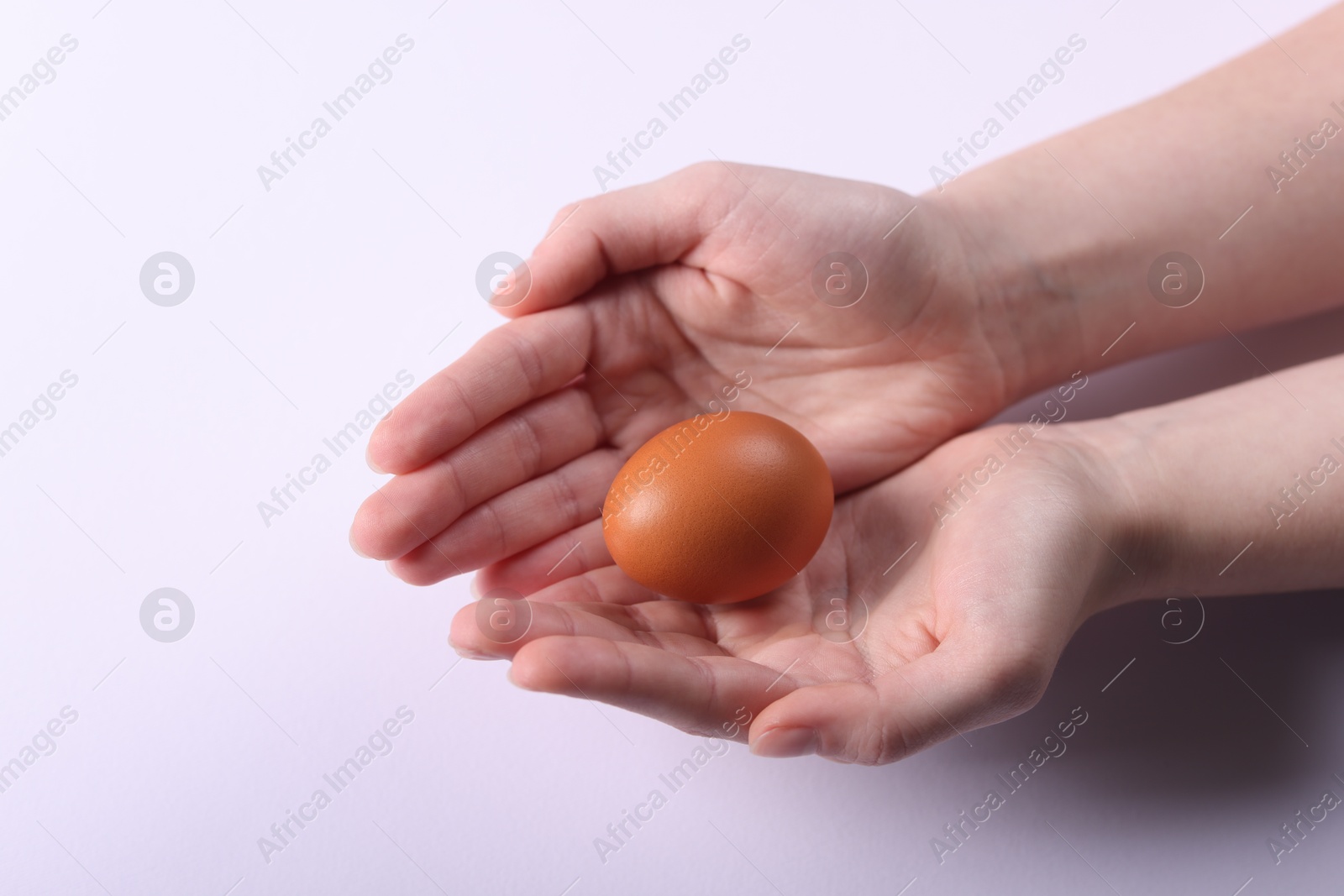 Photo of Woman holding raw egg on light background, closeup