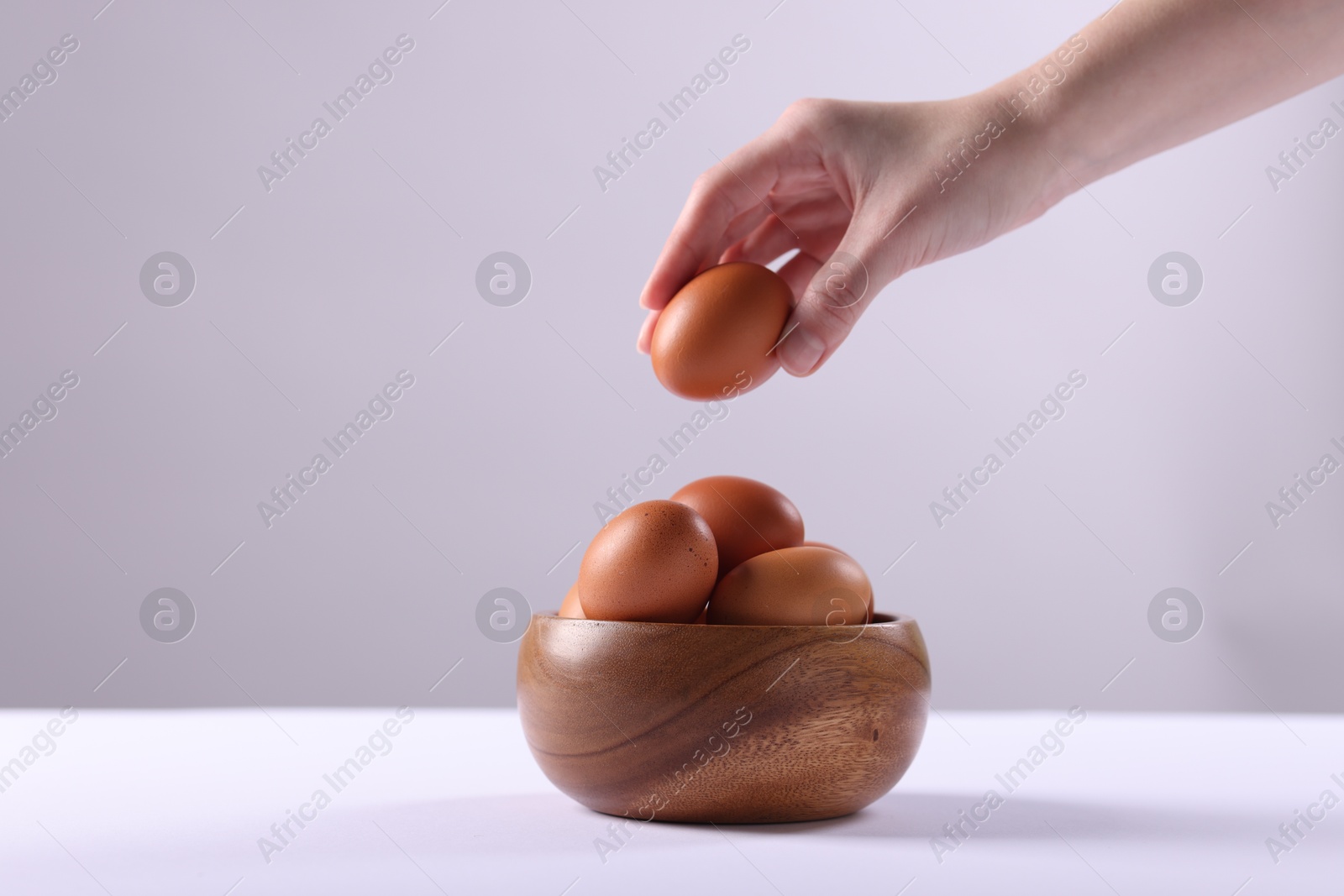 Photo of Woman taking raw egg from bowl at white table, closeup. Space for text