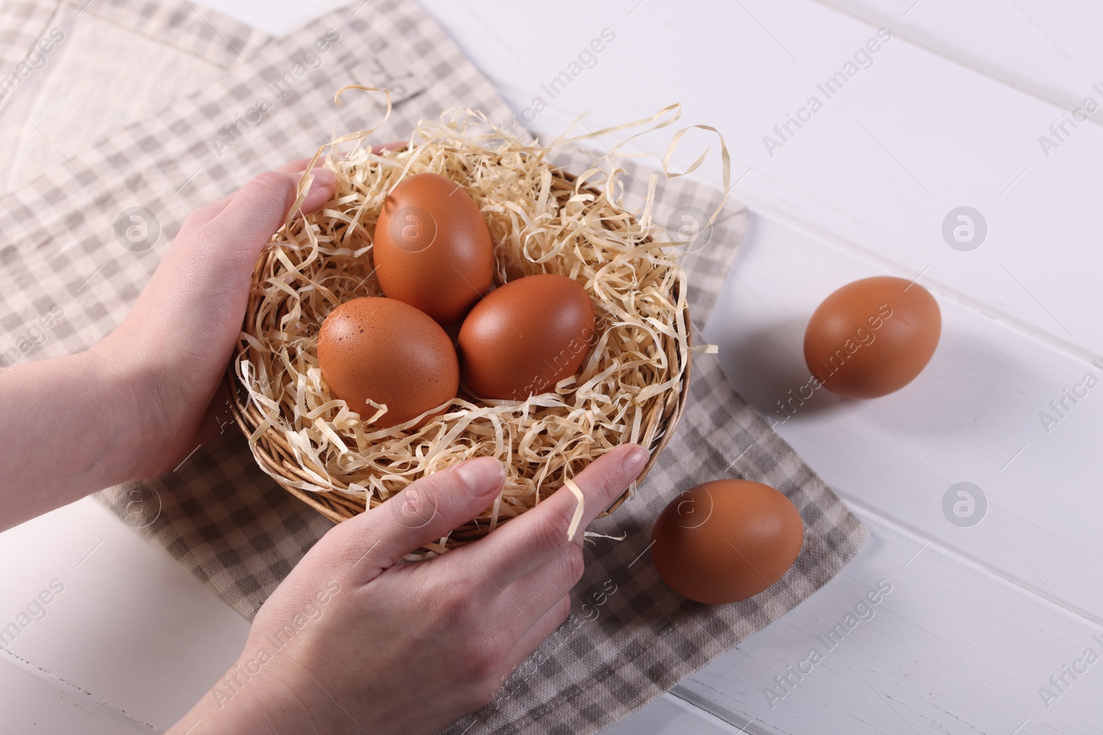 Photo of Woman with basket of raw eggs at white wooden table, closeup