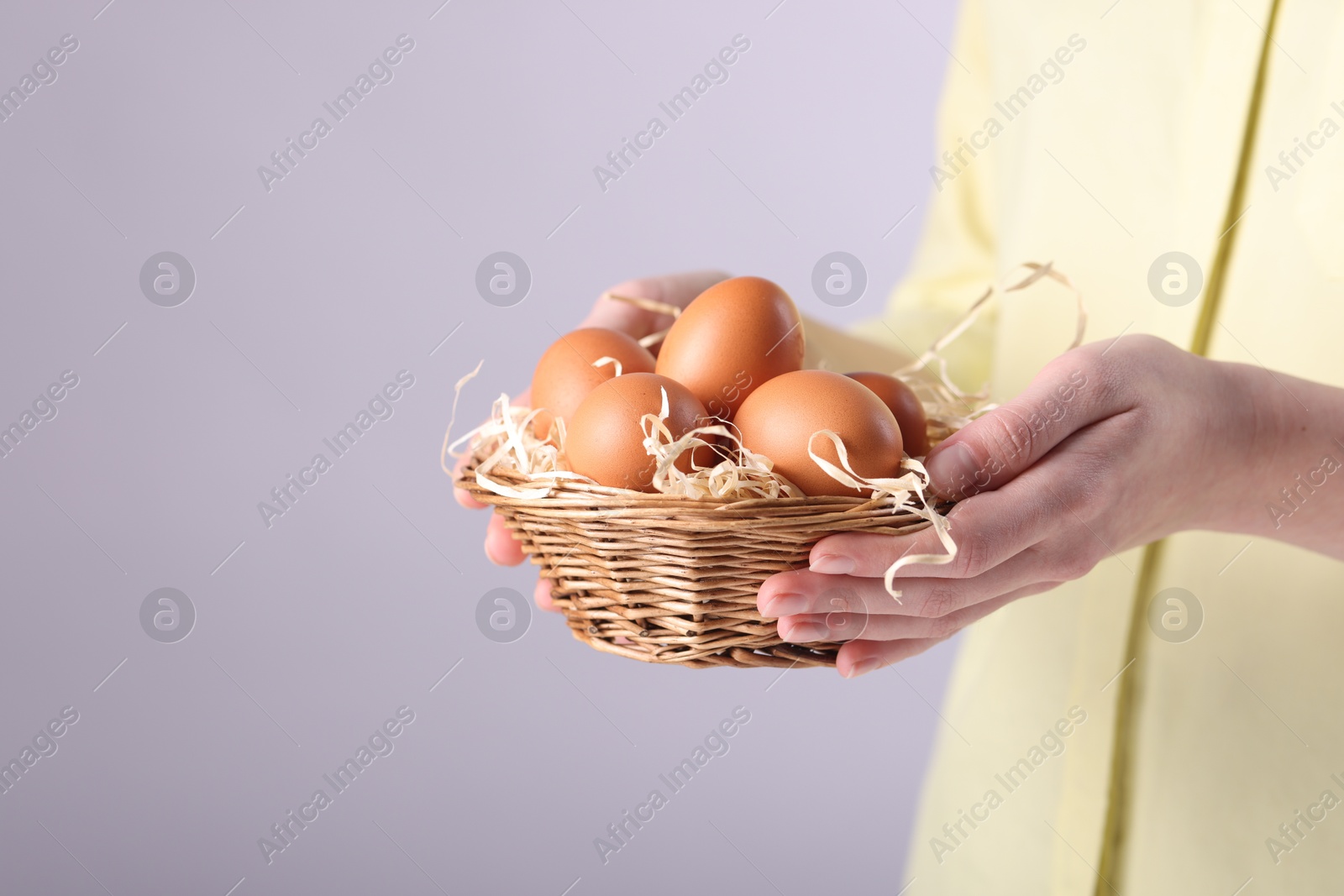 Photo of Woman with basket of raw eggs on light background, closeup. Space for text