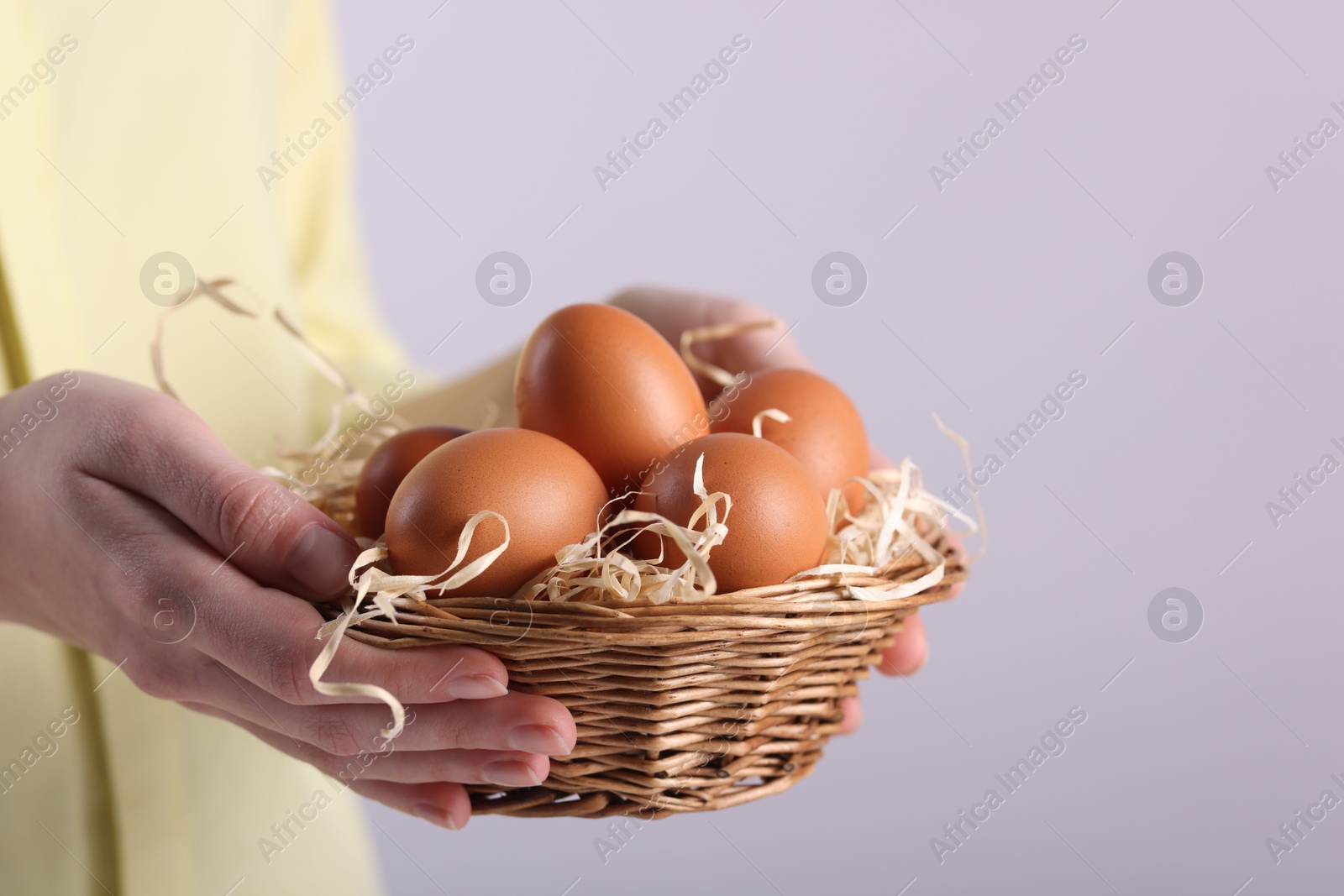 Photo of Woman with basket of raw eggs on light background, closeup. Space for text