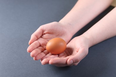 Photo of Woman with raw egg on grey background, closeup