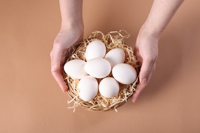 Photo of Woman with raw eggs on beige background, top view