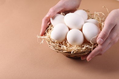 Photo of Woman with raw eggs on beige background, closeup. Space for text