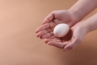 Photo of Woman holding raw egg on beige background, closeup. Space for text