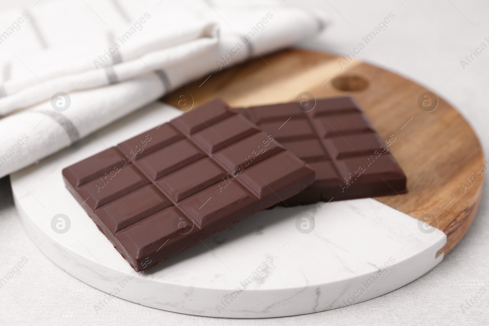 Photo of Pieces of delicious dark chocolate bar on light table, closeup