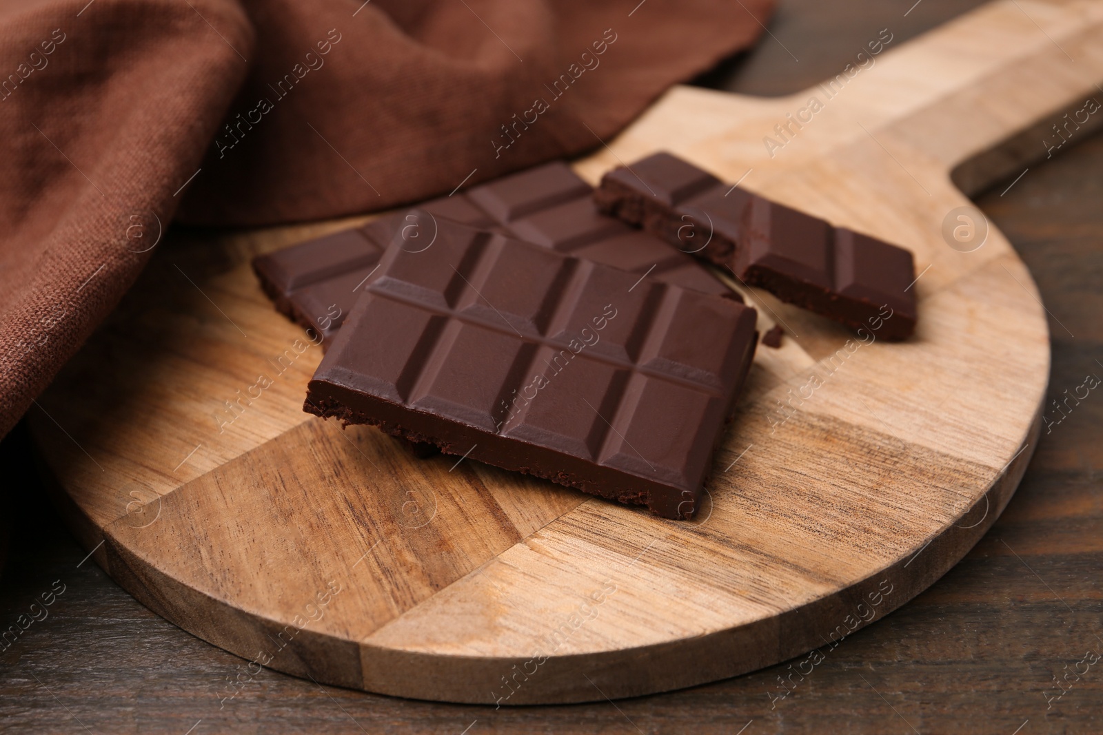 Photo of Pieces of delicious dark chocolate bar on wooden table, closeup