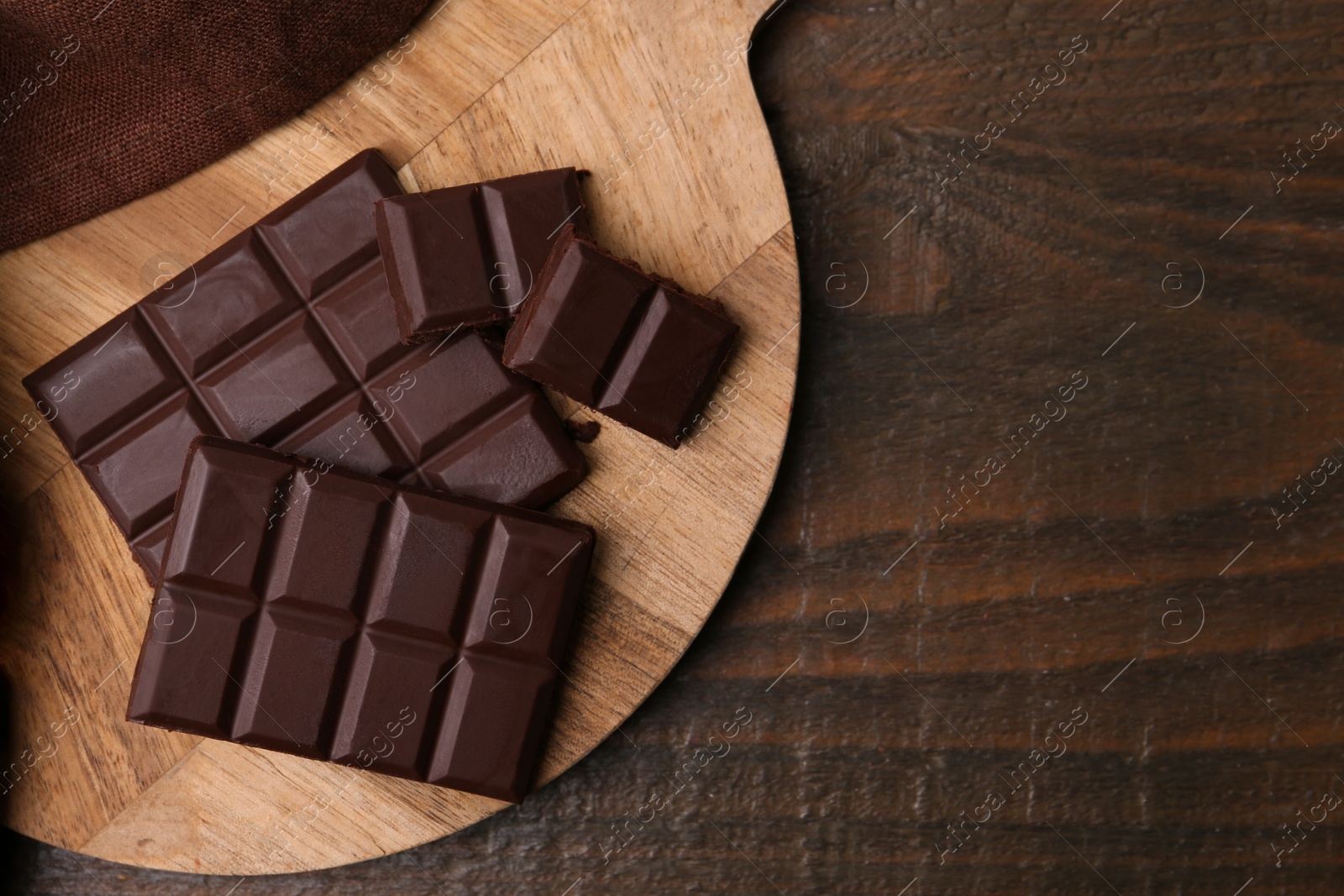 Photo of Pieces of delicious dark chocolate bar on wooden table, top view. Space for text