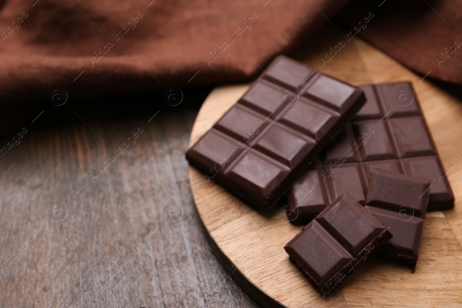 Photo of Pieces of delicious dark chocolate bar on wooden table, closeup. Space for text