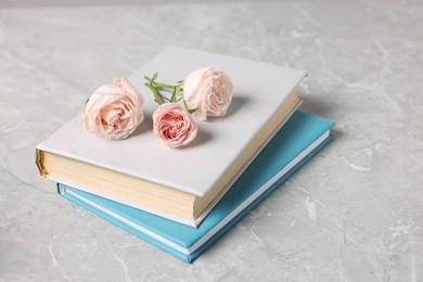 Photo of Books and beautiful rose flowers on gray marble table, closeup