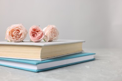 Photo of Books and beautiful rose flowers on gray marble table, closeup