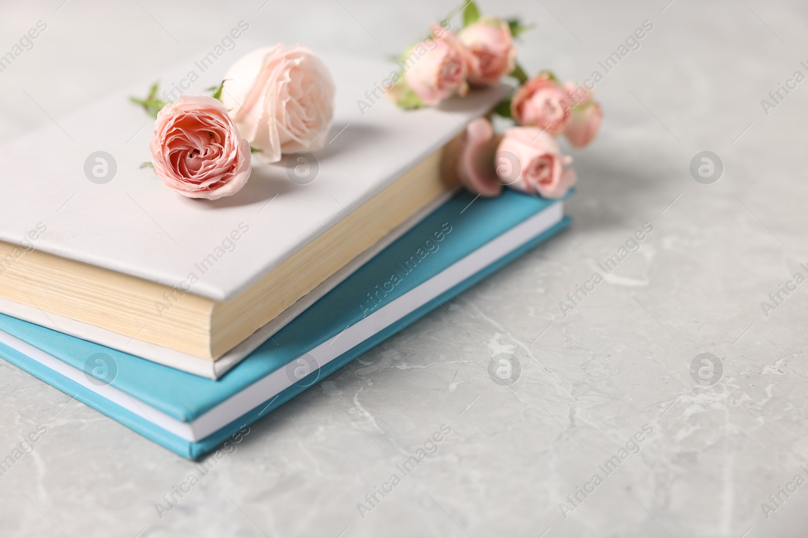 Photo of Books and beautiful rose flowers on gray marble table, closeup. Space for text