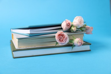 Photo of Books and beautiful rose flowers on light blue background, closeup