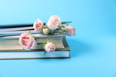 Photo of Books and beautiful rose flowers on light blue background, closeup. Space for text