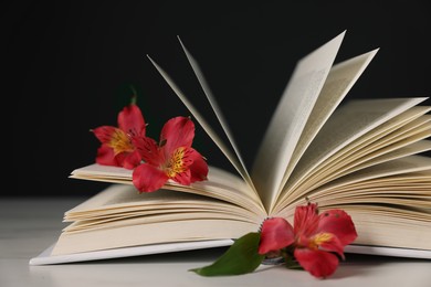 Photo of Book and beautiful alstroemeria flowers on light table against black background, closeup