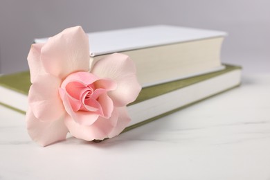 Photo of Books and beautiful rose flower on white marble table, closeup