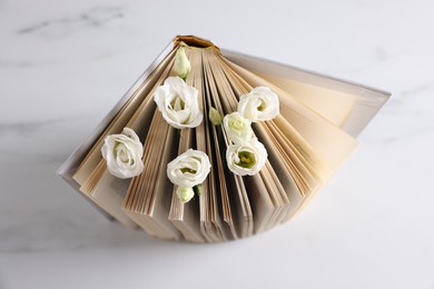 Photo of Book and beautiful eustoma flowers on white table, above view