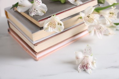 Photo of Books and beautiful alstroemeria flowers on white marble table, closeup