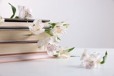 Photo of Books and beautiful alstroemeria flowers on white table against light background, closeup. Space for text