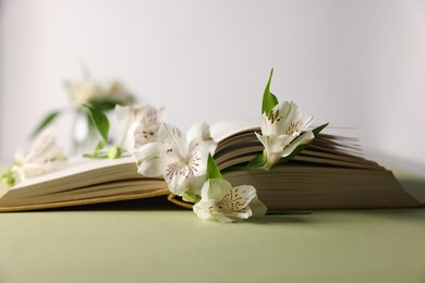 Book and beautiful alstroemeria flowers on green table against light background, closeup