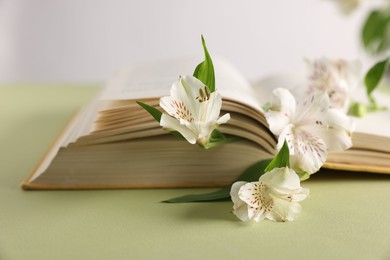 Book and beautiful alstroemeria flowers on green table against light background, closeup