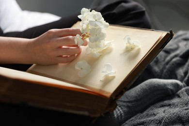 Photo of Woman reading book with beautiful flowers on blanket, closeup