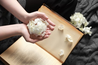 Photo of Woman holding pile of flower buds above book on blanket, top view