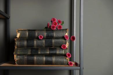 Stack of books and beautiful flowers on shelf near grey wall